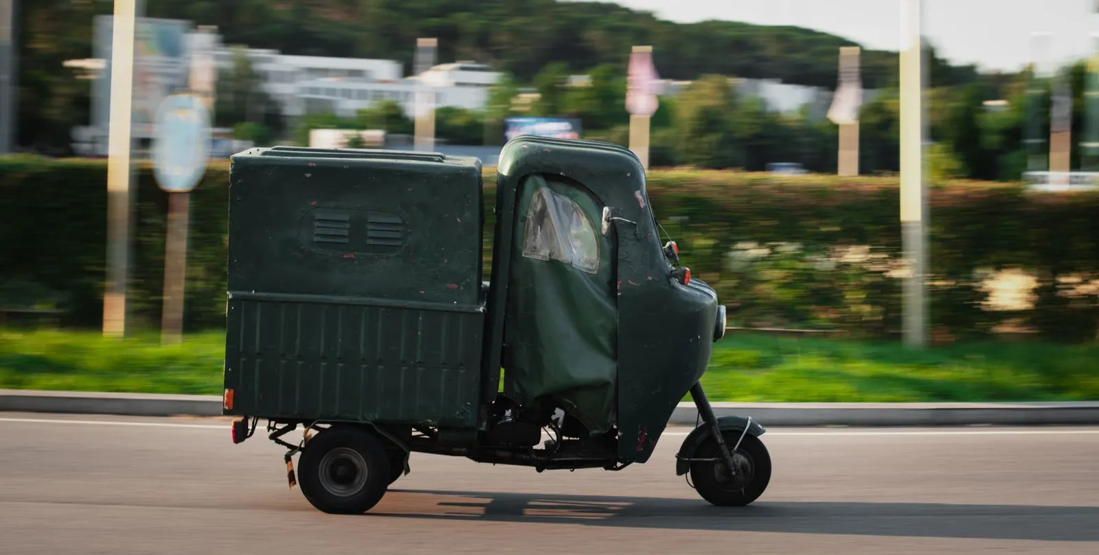 Un'Ape furgonata verde scuro in corsa su una strada