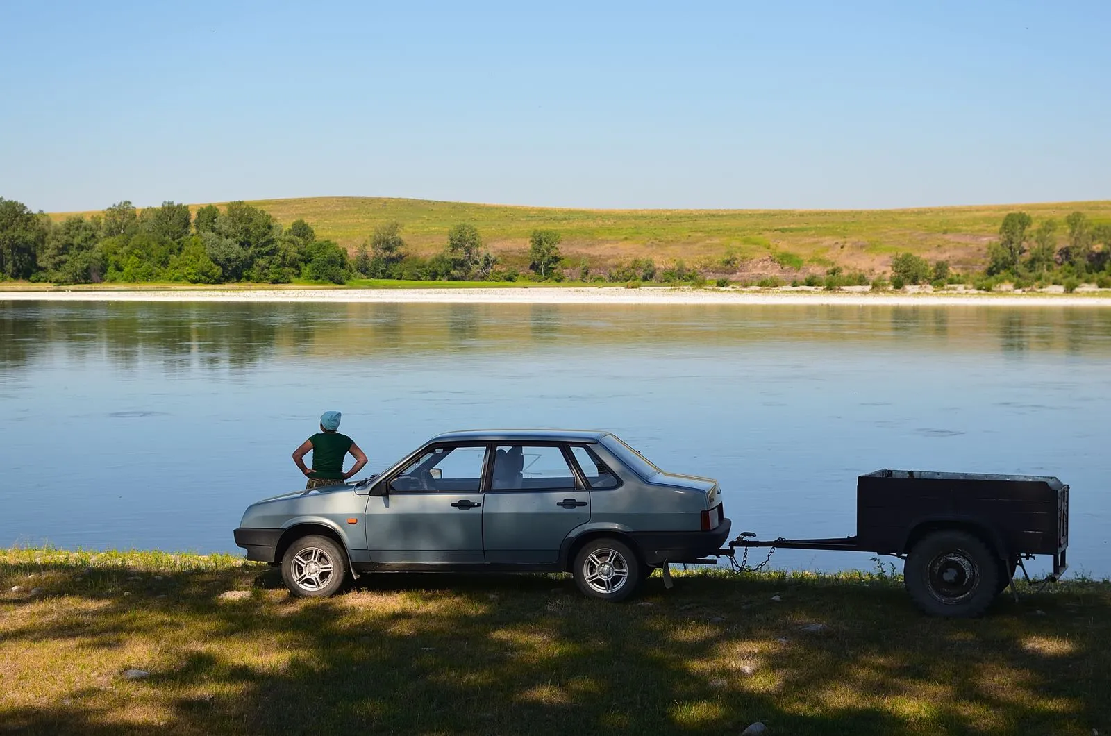 Una berlina grigia con un carrello piccolo, in riva a un lago