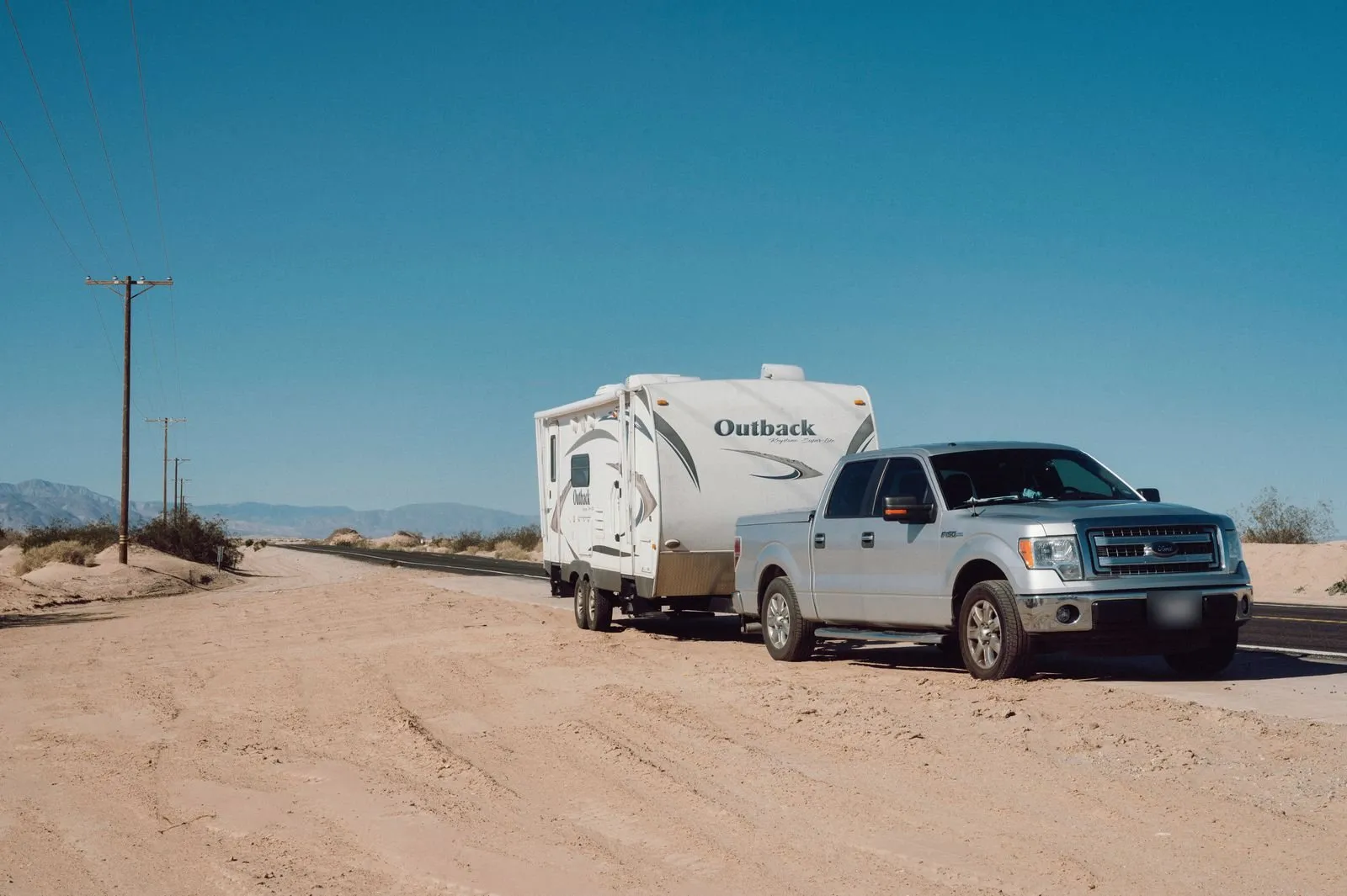 Un pick-up grigio che traina una roulotte grande su una strada nel deserto