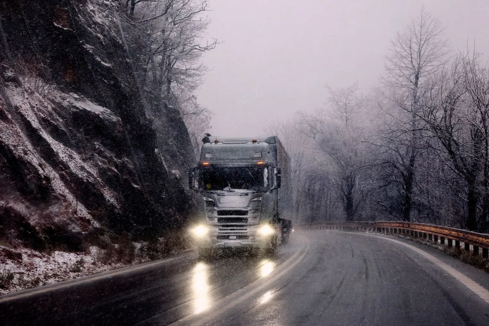 Un autoarticolato coi fari accesi su una strada di montagna innevata