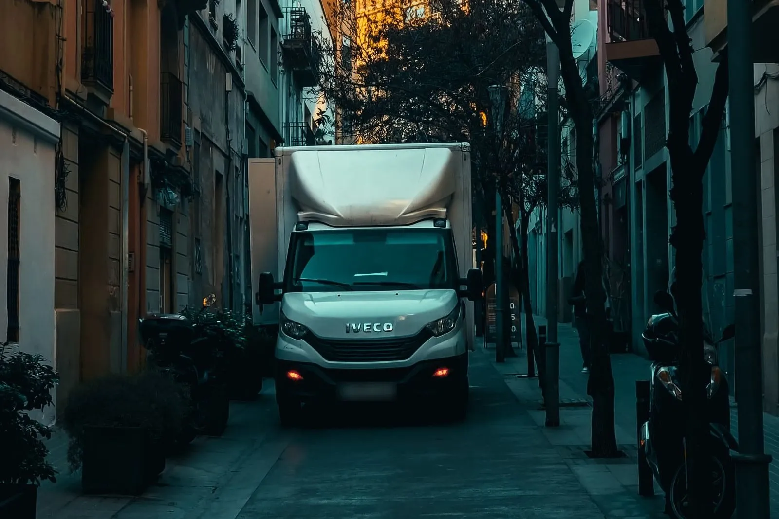 Un camion leggero furgonato bianco in una via stretta di città
