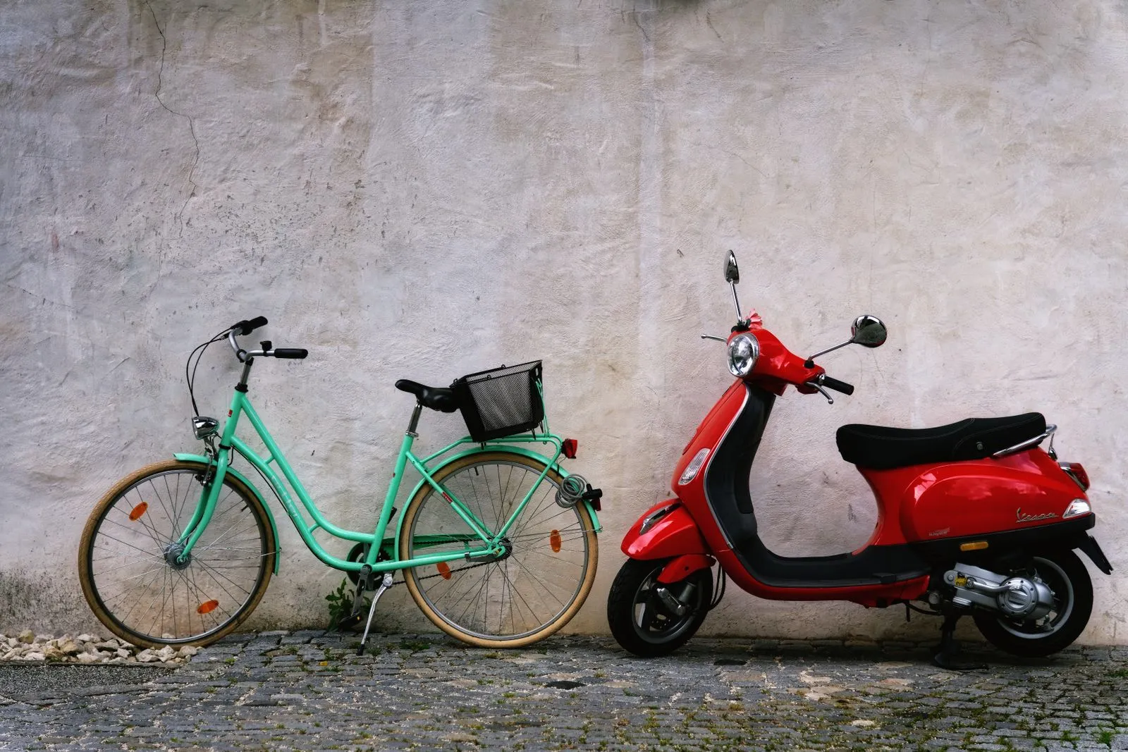 Uno scooter rosso parcheggiato accanto a una bicicletta, contro un muro chiaro