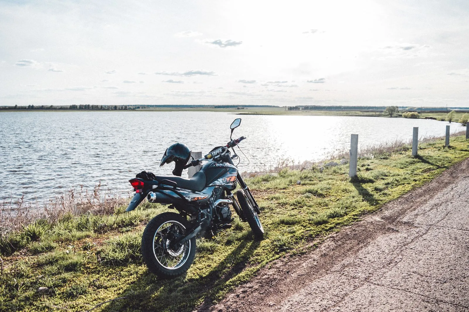 Una moto da strada parcheggiata sul prato in riva a un lago, col casco sulla sella
