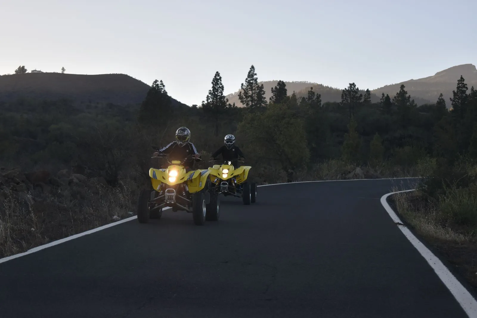 Due quad coi fari accesi su una strada di montagna, guidati da piloti col casco