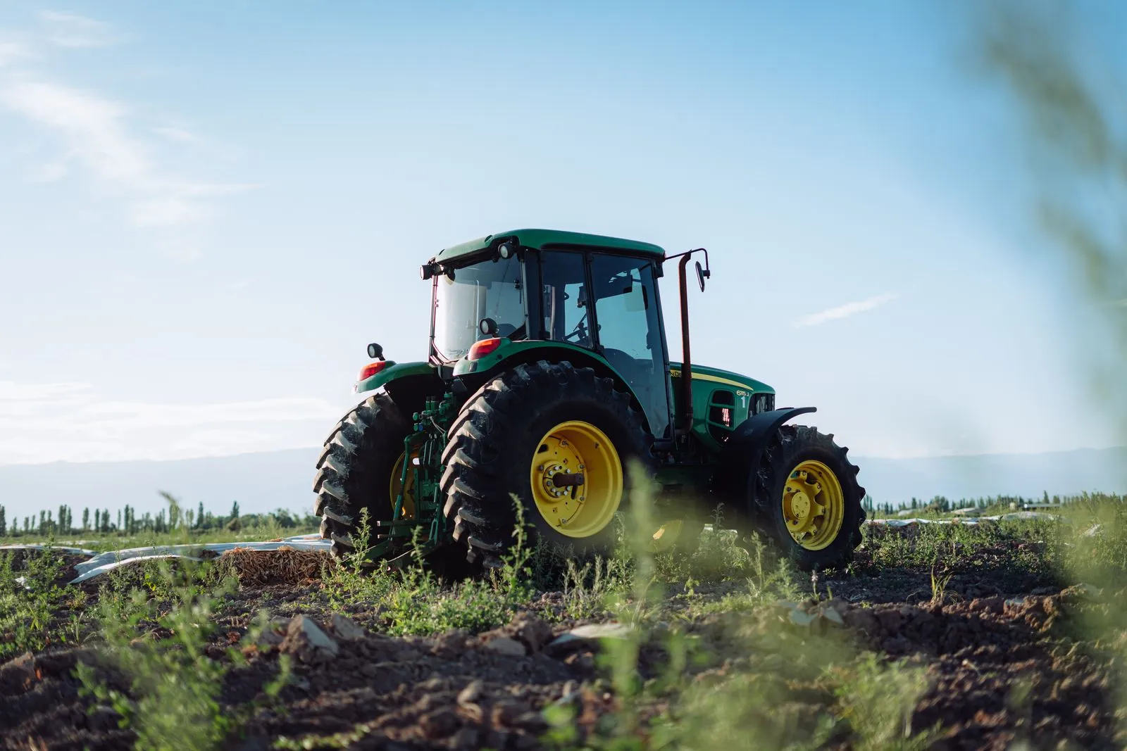 Un trattore verde con le ruote gialle in un campo arato
