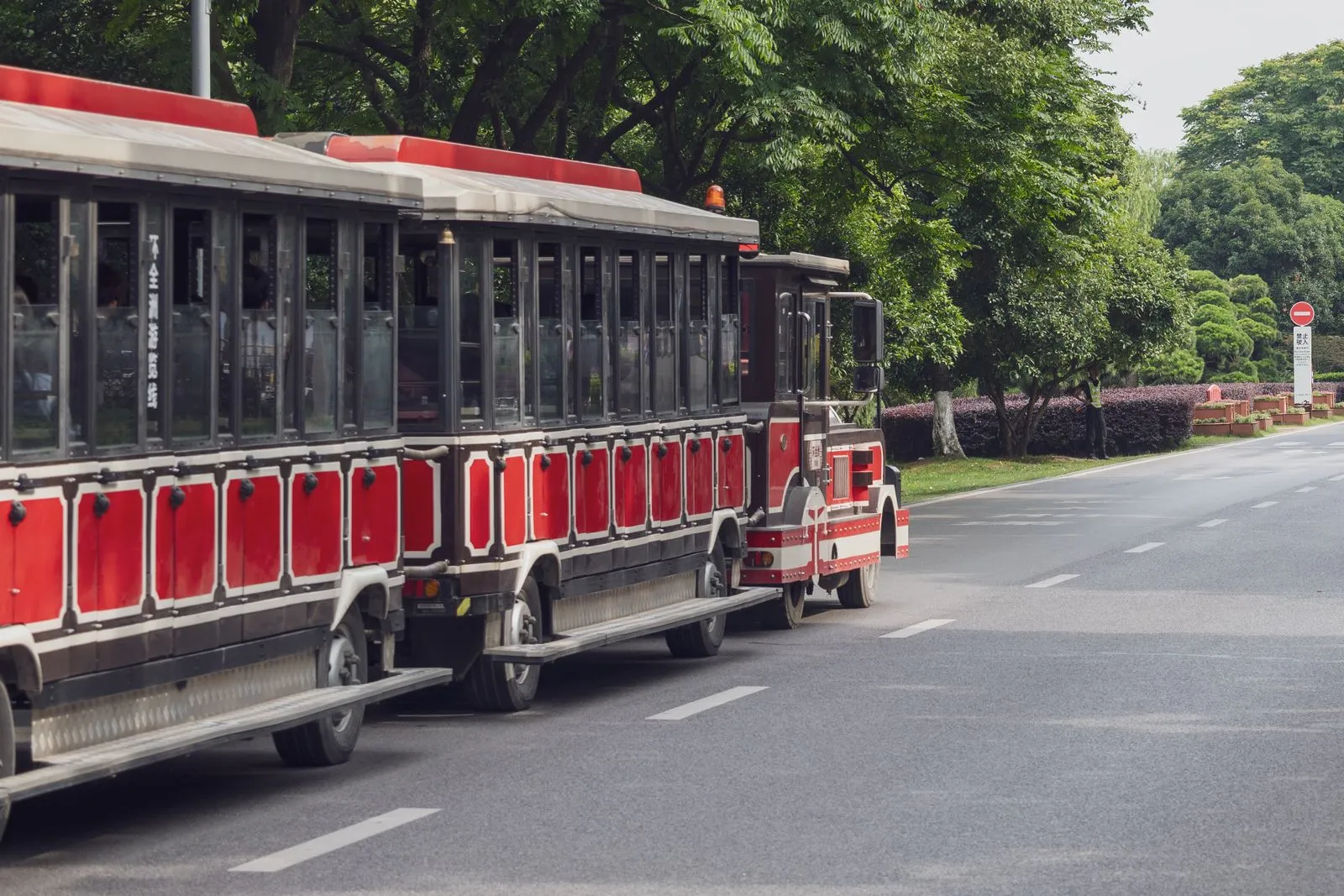Un trenino turistico rosso su gomma, fermo su una strada alberata