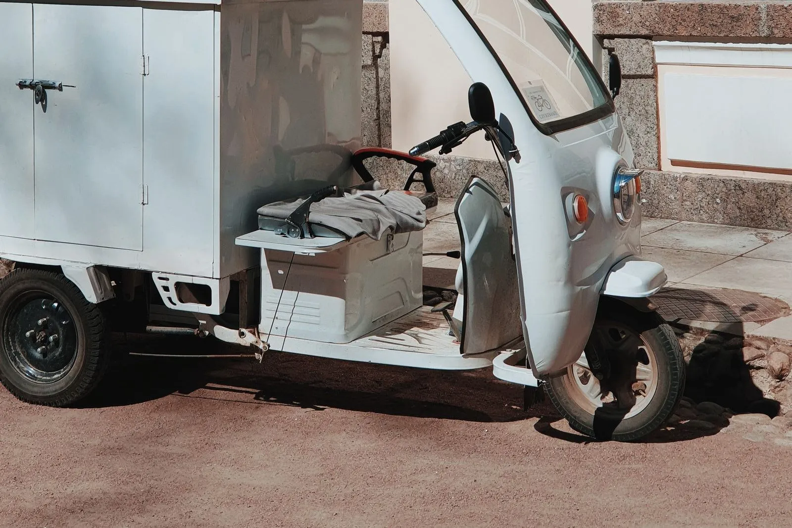 Un piccolo triciclo elettrico da carico, bianco, col cassone chiuso